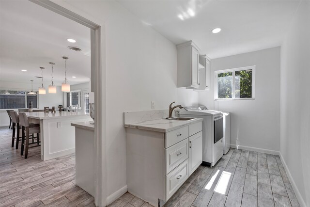 laundry area with light hardwood / wood-style floors, cabinets, independent washer and dryer, and sink