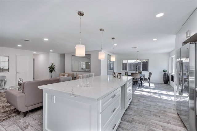 kitchen featuring light wood-type flooring, a kitchen island, pendant lighting, white cabinets, and stainless steel refrigerator