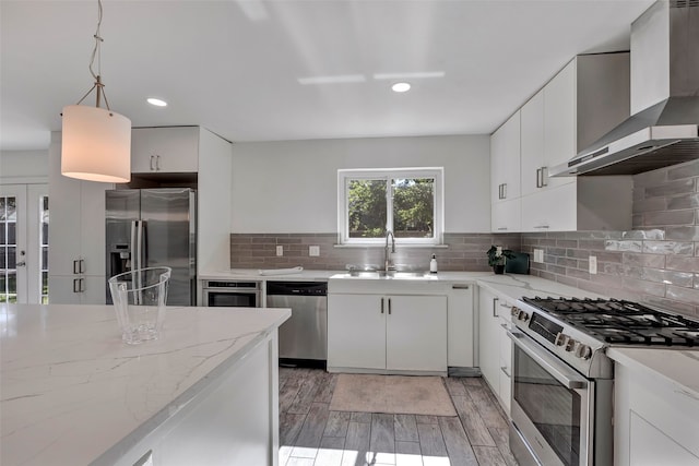 kitchen with white cabinetry, sink, hanging light fixtures, wall chimney range hood, and appliances with stainless steel finishes