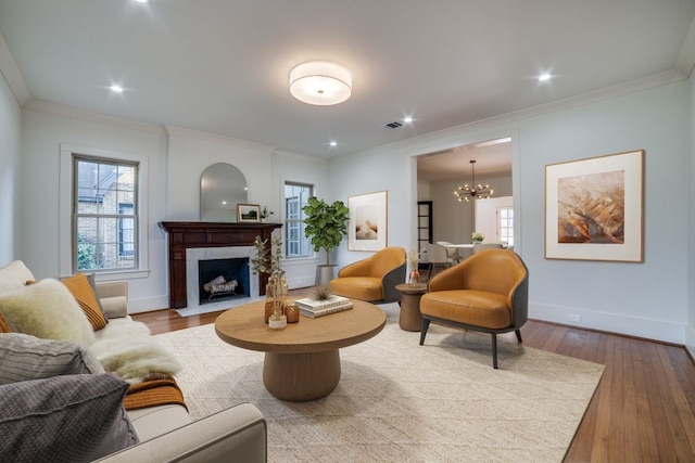 living room featuring hardwood / wood-style floors, a tile fireplace, crown molding, and a notable chandelier