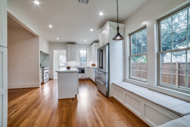 kitchen with white cabinetry, high end appliances, decorative light fixtures, and a healthy amount of sunlight