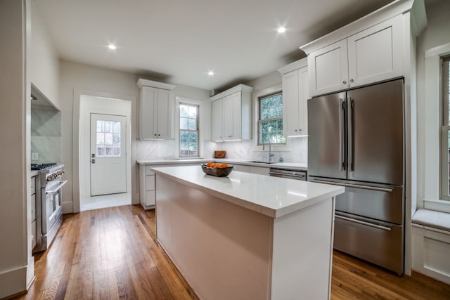 kitchen featuring wood-type flooring, a center island, white cabinets, decorative backsplash, and high quality appliances