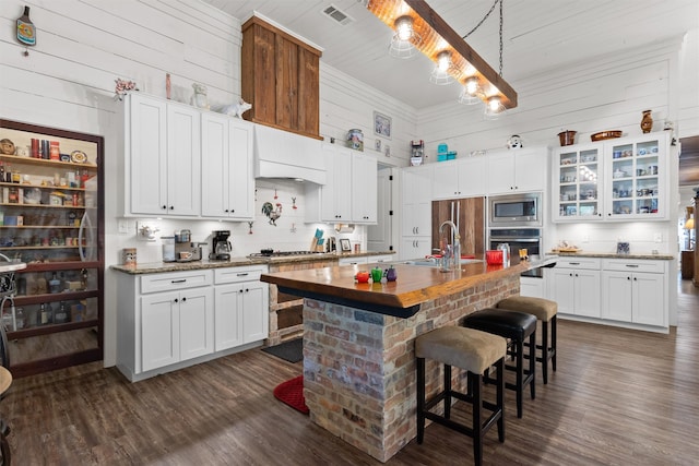 kitchen featuring a kitchen bar, custom range hood, stainless steel appliances, a kitchen island with sink, and white cabinetry