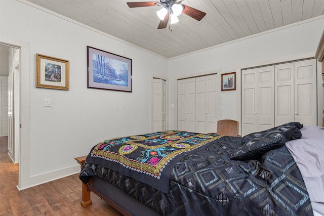 bedroom featuring ceiling fan, dark hardwood / wood-style flooring, wood ceiling, two closets, and ornamental molding