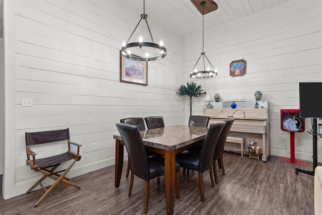 dining room with wooden walls, a notable chandelier, and dark hardwood / wood-style flooring