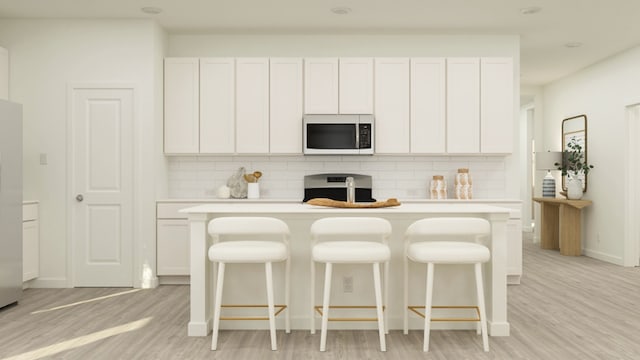 kitchen featuring backsplash, light hardwood / wood-style flooring, white cabinets, stainless steel stove, and an island with sink