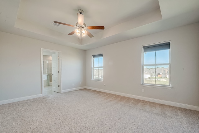 unfurnished room with a tray ceiling, light carpet, and ceiling fan