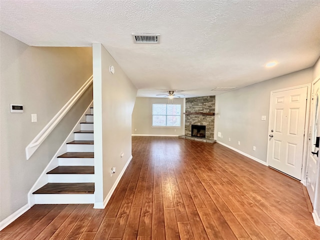 unfurnished living room featuring wood-type flooring, a textured ceiling, and a stone fireplace