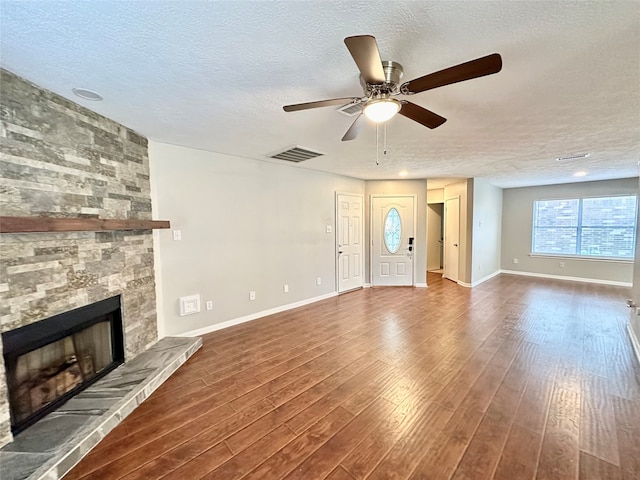 unfurnished living room with a stone fireplace, hardwood / wood-style floors, a textured ceiling, and ceiling fan