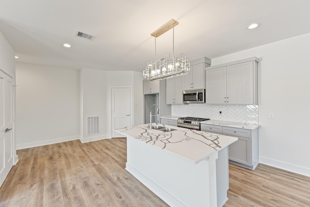 kitchen with sink, hanging light fixtures, a center island with sink, appliances with stainless steel finishes, and light wood-type flooring