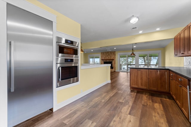 kitchen with stainless steel appliances, dark hardwood / wood-style flooring, kitchen peninsula, a large fireplace, and decorative light fixtures