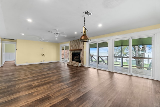 unfurnished living room with a stone fireplace, dark wood-type flooring, and ceiling fan