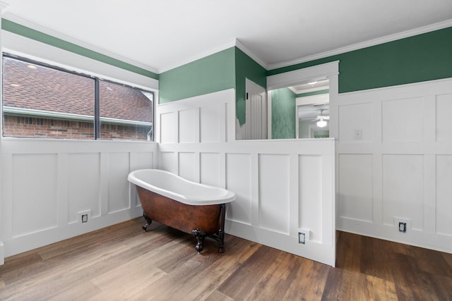 bathroom with wood finished floors, ceiling fan, a freestanding bath, crown molding, and a decorative wall