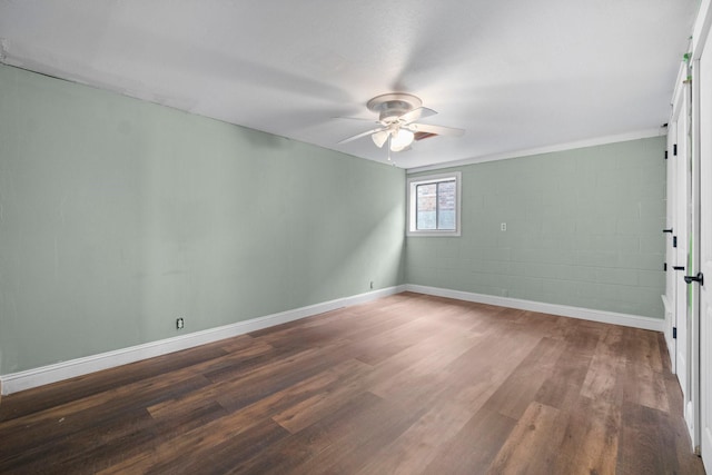 spare room with concrete block wall, dark wood-style floors, baseboards, and ceiling fan