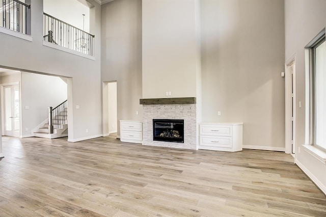 unfurnished living room with a towering ceiling, a stone fireplace, and light hardwood / wood-style flooring