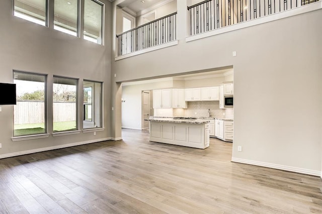 unfurnished living room with a towering ceiling, sink, and light hardwood / wood-style flooring