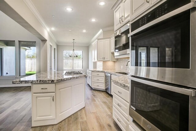 kitchen featuring decorative light fixtures, white cabinets, a center island, stainless steel appliances, and light hardwood / wood-style flooring