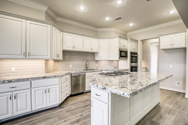 kitchen with appliances with stainless steel finishes, white cabinetry, sink, a center island, and light stone countertops