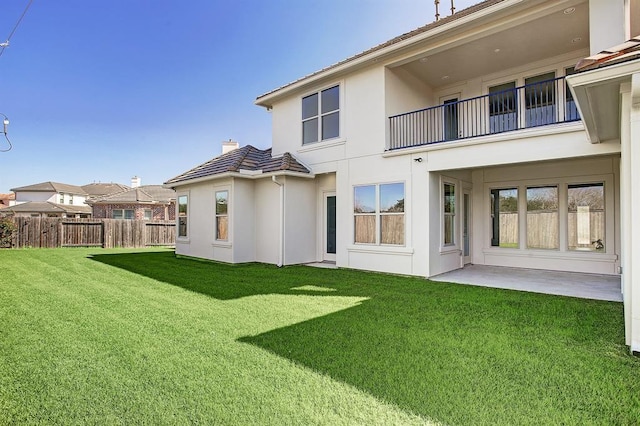 rear view of house with a balcony, fence, a lawn, stucco siding, and a chimney