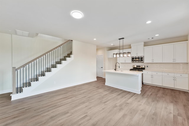 kitchen featuring appliances with stainless steel finishes, decorative light fixtures, white cabinetry, and light hardwood / wood-style flooring