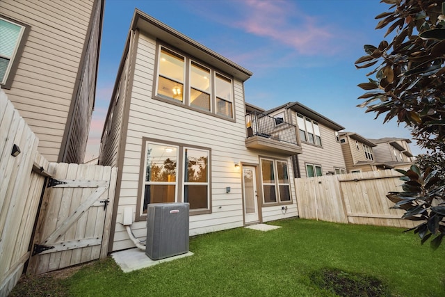 back house at dusk featuring cooling unit, a yard, and a balcony