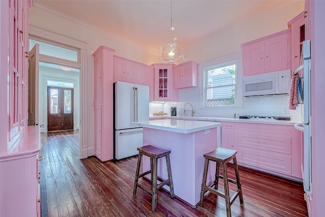 kitchen with backsplash, hanging light fixtures, white appliances, a kitchen island, and dark hardwood / wood-style flooring