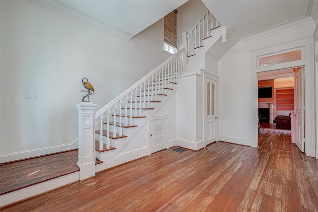 stairs featuring a towering ceiling, wood-type flooring, and ornamental molding