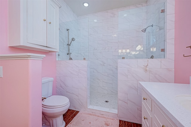 bathroom with tile walls, vanity, toilet, and a tile shower