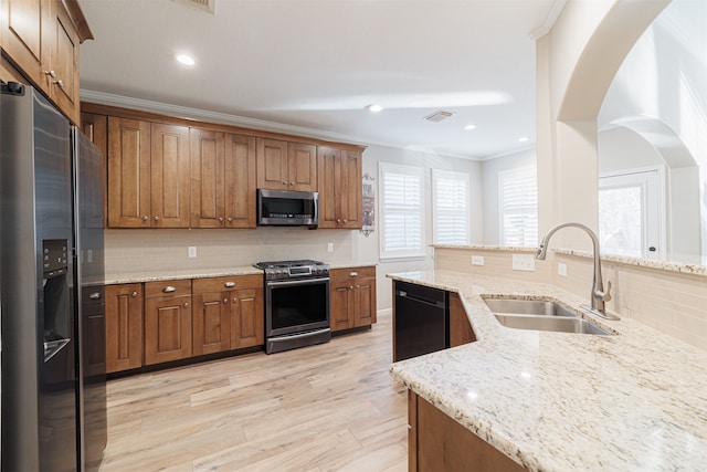 kitchen with backsplash, sink, light wood-type flooring, light stone countertops, and appliances with stainless steel finishes