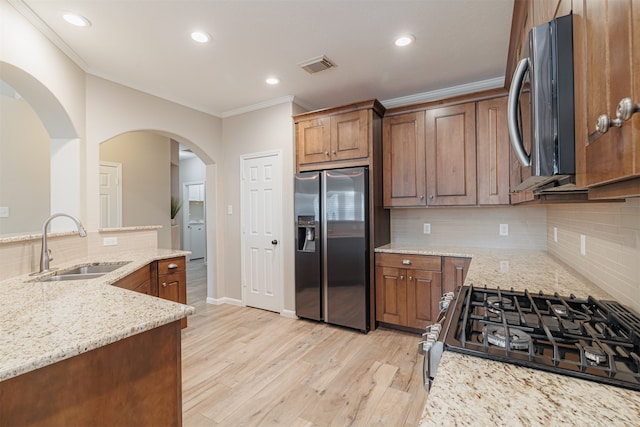 kitchen with sink, decorative backsplash, light wood-type flooring, light stone counters, and stainless steel appliances