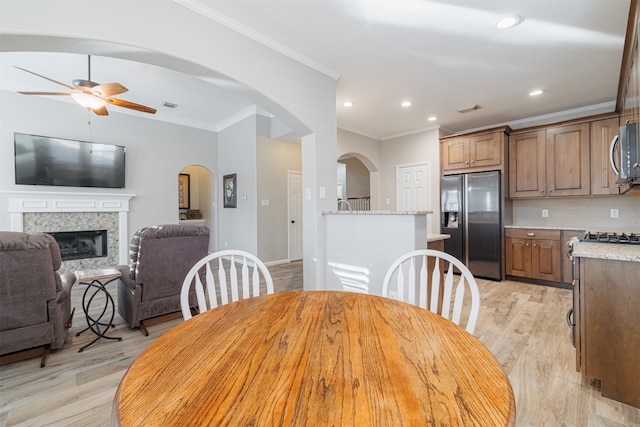 dining space with a fireplace, light hardwood / wood-style floors, ceiling fan, and ornamental molding