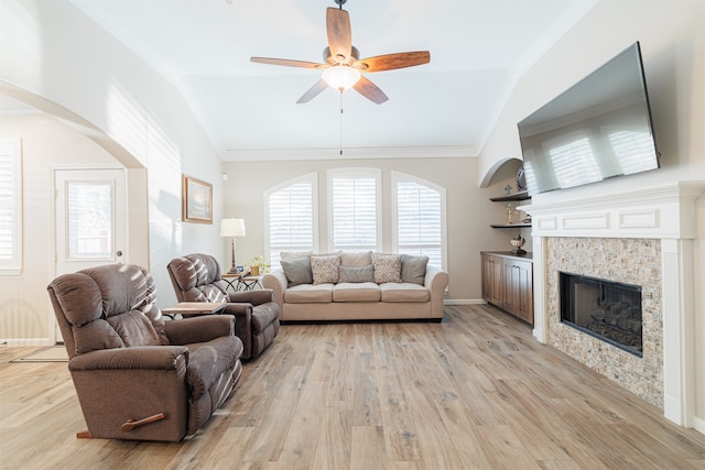 living room featuring light wood-type flooring, a stone fireplace, ceiling fan, and vaulted ceiling