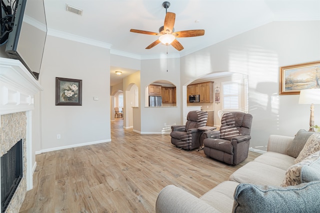 living room with ceiling fan, light hardwood / wood-style floors, a stone fireplace, and crown molding