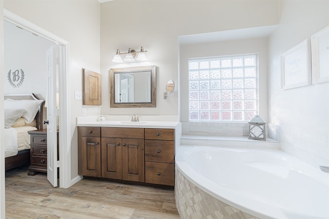 bathroom with vanity, a relaxing tiled tub, and wood-type flooring