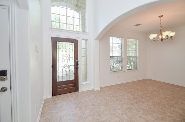 foyer entrance featuring a chandelier, light tile patterned floors, crown molding, and plenty of natural light