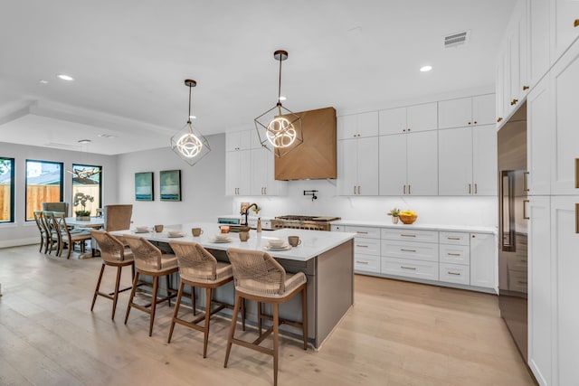 kitchen with a kitchen bar, light wood-type flooring, white cabinetry, and a kitchen island with sink