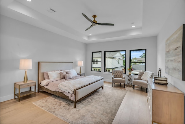 bedroom with ceiling fan, light wood-type flooring, and a tray ceiling