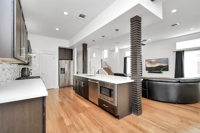 kitchen with sink, an island with sink, tasteful backsplash, light hardwood / wood-style floors, and stainless steel appliances