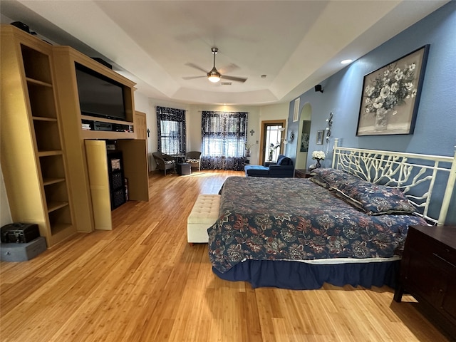 bedroom with a raised ceiling, ceiling fan, and light wood-type flooring