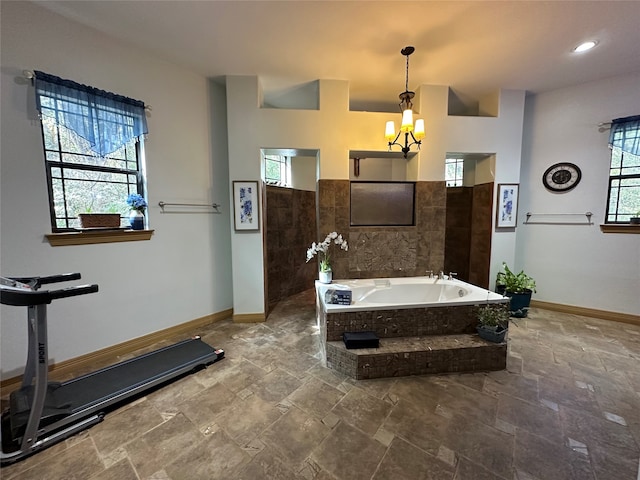 bathroom with a chandelier, a relaxing tiled tub, and a healthy amount of sunlight