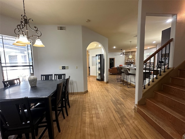 dining space with ceiling fan with notable chandelier and light wood-type flooring