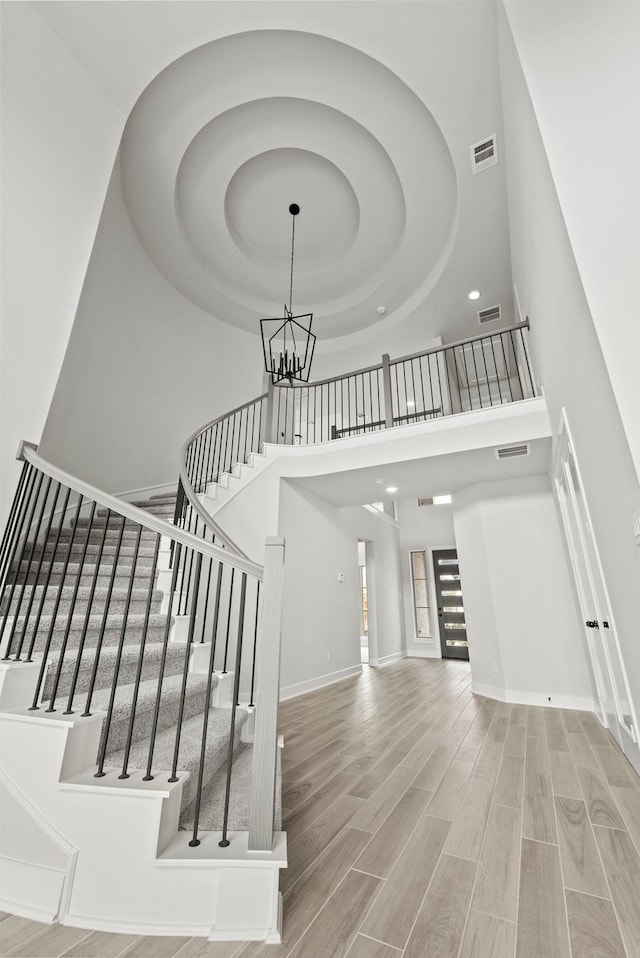 staircase featuring wood-type flooring, a high ceiling, and a notable chandelier