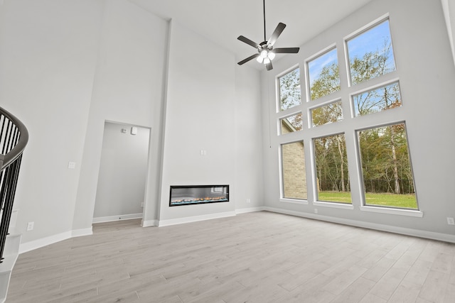 unfurnished living room featuring a towering ceiling, plenty of natural light, ceiling fan, and light hardwood / wood-style flooring