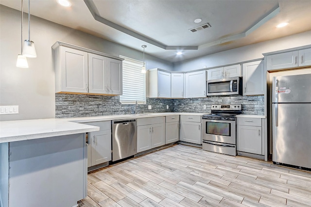 kitchen featuring gray cabinetry, a raised ceiling, decorative light fixtures, light hardwood / wood-style floors, and stainless steel appliances