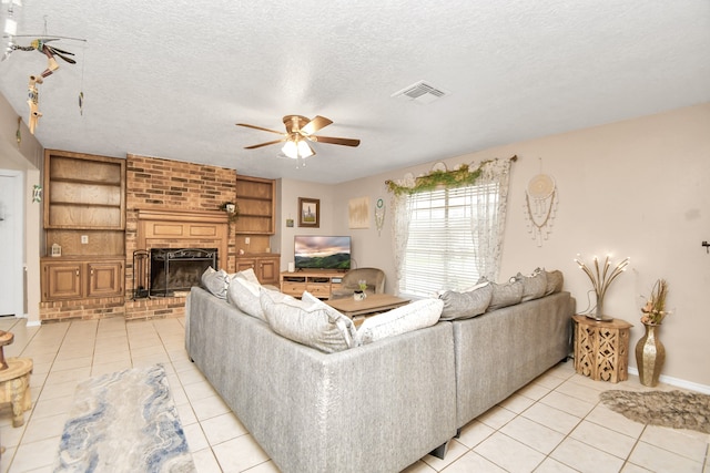 living room featuring ceiling fan, a fireplace, light tile patterned flooring, and a textured ceiling