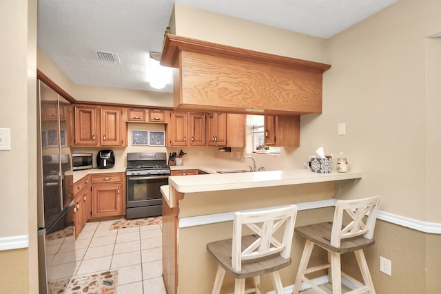 kitchen with sink, kitchen peninsula, a breakfast bar, light tile patterned floors, and appliances with stainless steel finishes