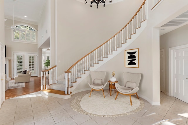 entryway featuring french doors, a towering ceiling, crown molding, an inviting chandelier, and light hardwood / wood-style floors