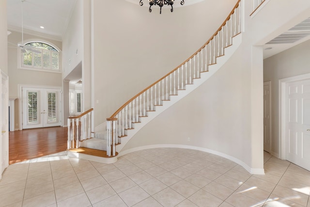 entryway featuring light hardwood / wood-style flooring, a notable chandelier, crown molding, french doors, and a towering ceiling