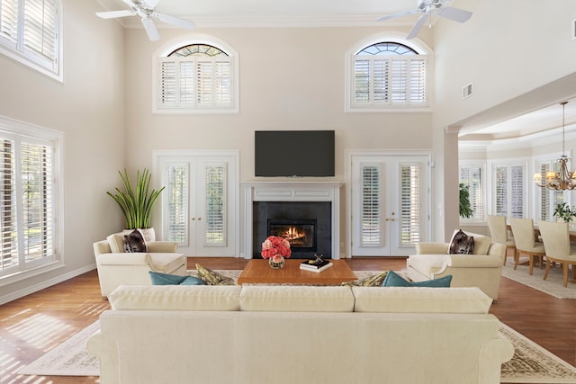 living room with ceiling fan with notable chandelier, a towering ceiling, hardwood / wood-style flooring, and ornamental molding