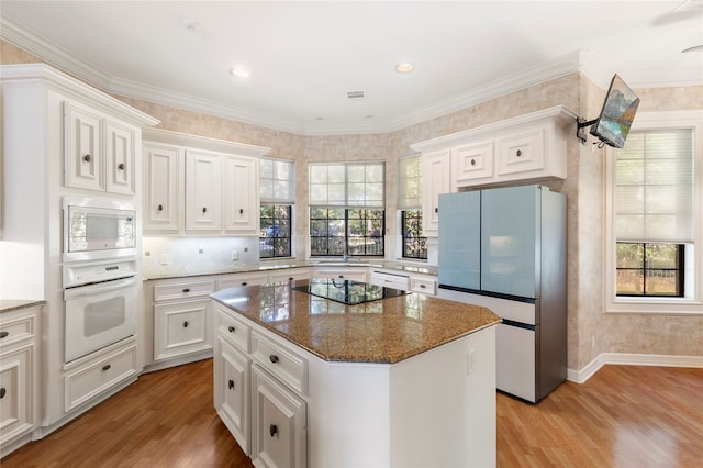 kitchen with appliances with stainless steel finishes, light wood-type flooring, white cabinetry, and dark stone counters